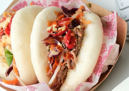 two bao buns in wrapping paper on a plate