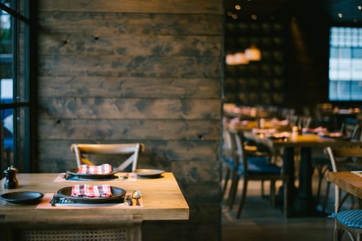 Interior of a restaurant with wooden walls and a table and chair with table settings in the foreground