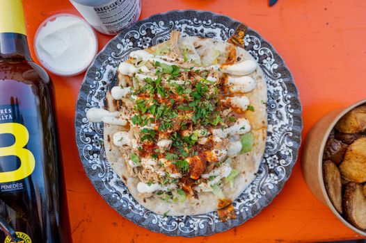 flat lay of a blue floral plate with flatbread, grilled meat and herbs and chillies, drizzled with aioli.