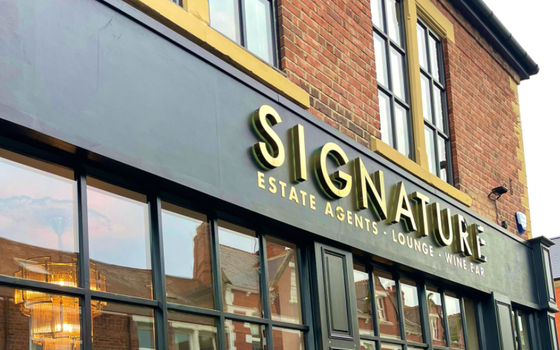 red brick building with a navy shop front that reads SIGNATURE - Estate Agents, Lounge, Wine Bar