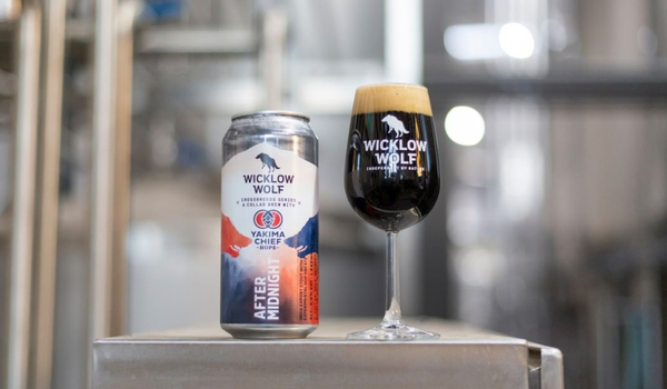 Can of Wicklow Wolf stout with small glass of the stout beside it. Out of focus, the brewery can be seen in the background