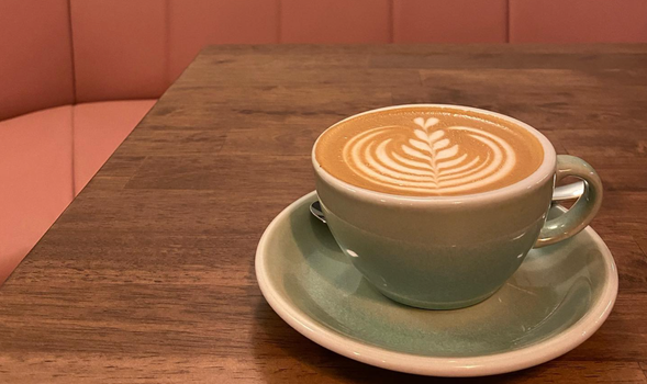 wooden table with a milky coffee with latte art in an aqua-coloured cup and saucer