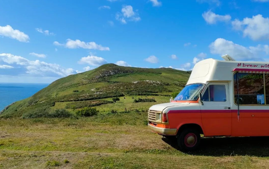 green field with a blue sky and orange and white coffee truck parked up