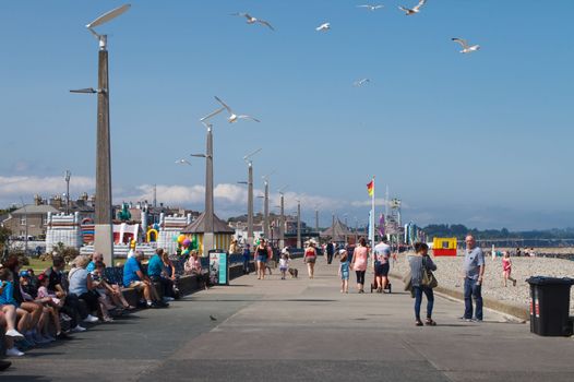 Bray seafront in the sun, people walking and sitting on the wall, seagulls, blue skies