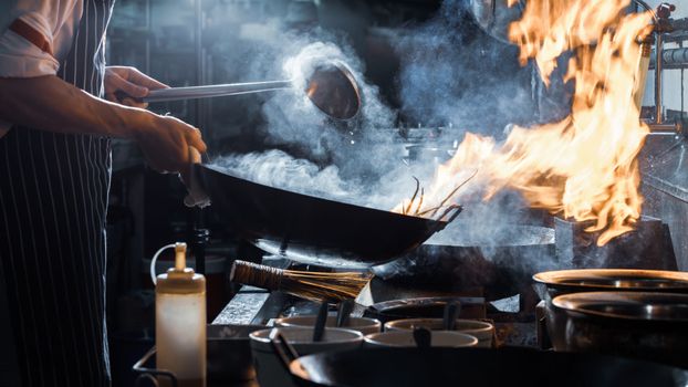 pan on a hob with flames coming from it on a hob in a restaurant kitchen, being tended to by a chef