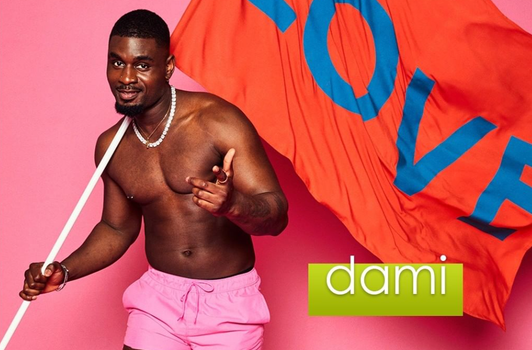 A man in pink swimshorts looking and gesturing to the camera, holding a large red flag with the word "love" written in blue. His name, Dami, appears in the corner