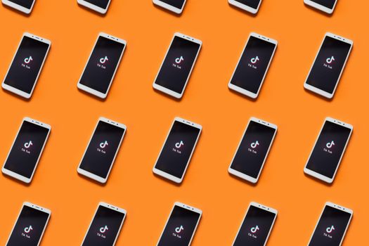 multiple phones on an orange background with the TikTok home screen showing on each phone
