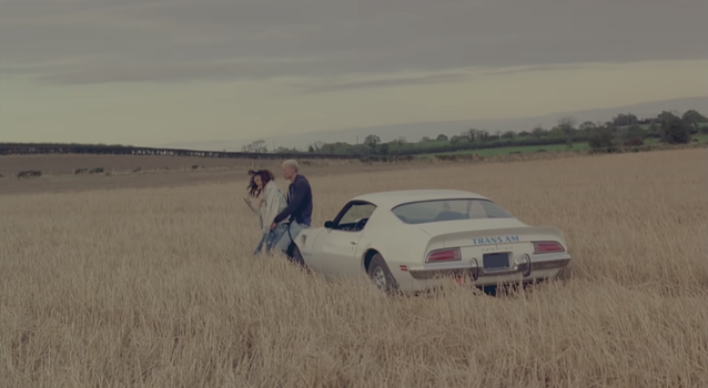 still from Rihanna's We Found Love Music video, Rihanna and her male co star in a barley field, leaning on a car