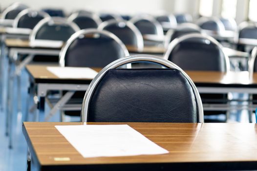exam hall with tables and chairs lined up, with an exam paper on each of them