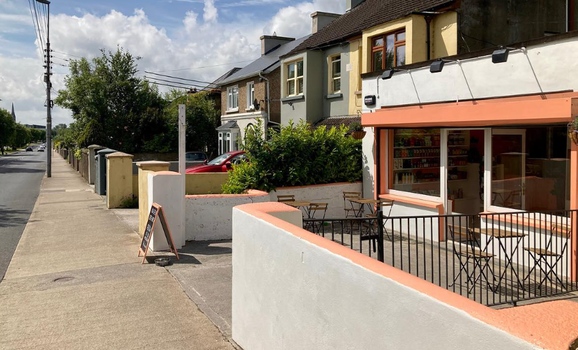 exterior of a white and peach coloured cafe with residential houses on the road behind it