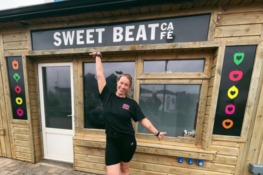 woman smiling outside a wooden panelled building with a sign reading "Sweet Beat Cafe"