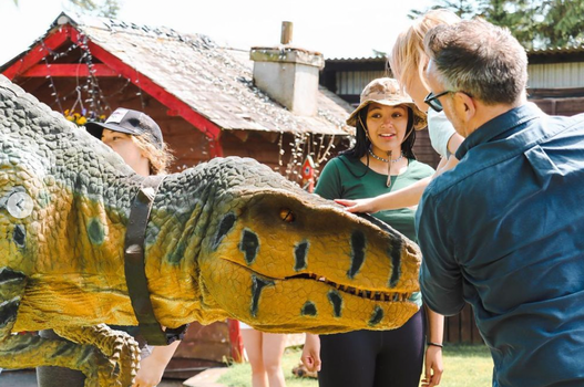 man holding a little girl up to pet a lifelike dinosaur replica