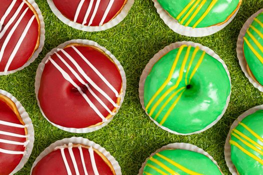 ring donuts displayed on a grassy background, half are red with white stripes and half are green with gold stripes
