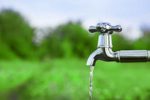 water coming from a silver tap, green field in background