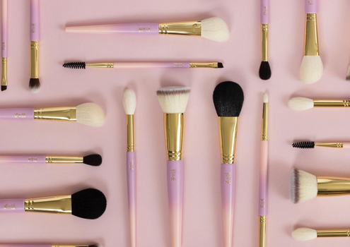 flat lay of mauve coloured makeup brushes on a light pink surface