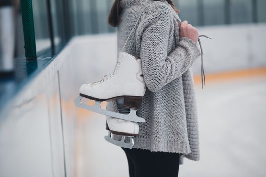 person on ice rink with ice skates being held over their shoulder by the laces