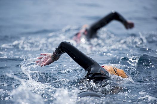 two people swimming in the sea in wetsuits and swimcaps