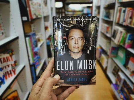 person in a bookshop holding up a book about elon musk