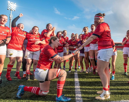 munster rugby player on one knee proposing to another as the rest of the team cheer in the background