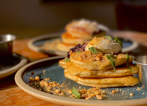 a stack of pancakes with cream, jam and other toppings on a plate at a café
