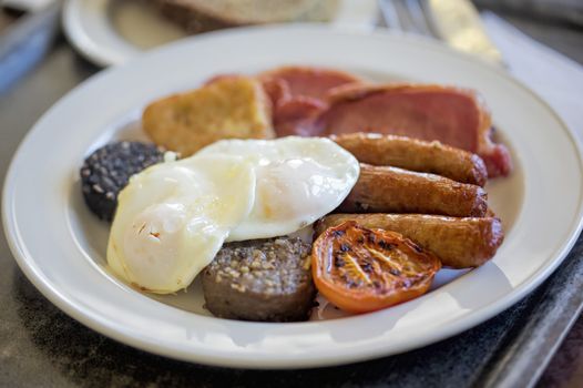 fry up breakfast on a plate with sausages, egg and pudding